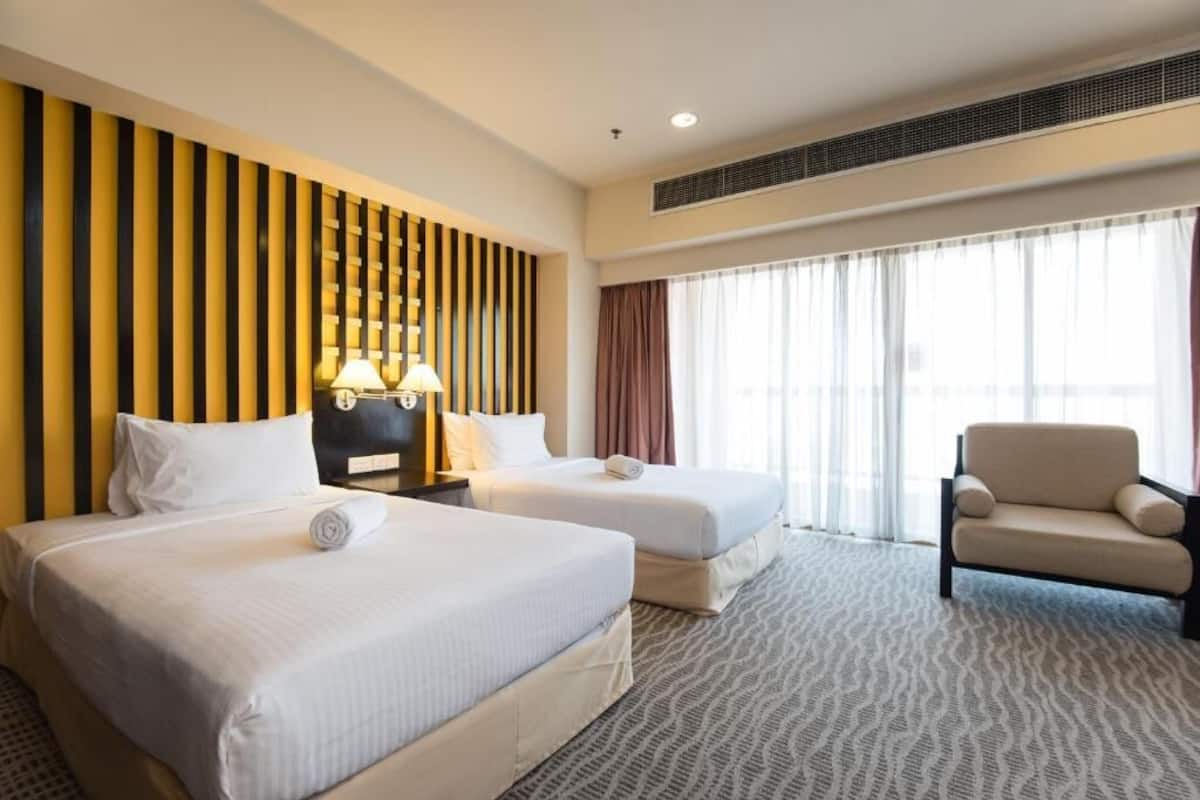 Une chambre d’hôtel avec deux lits, un canapé, une lampe et une grande fenêtre avec des rideaux.