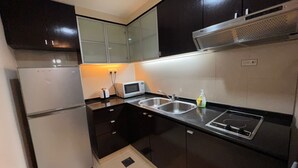 A compact kitchen with dark cabinetry, a built-in microwave, a stainless steel sink, and a gas stove. - Raintree Resort suites at Bandar Sunway (Petaling Jaya)