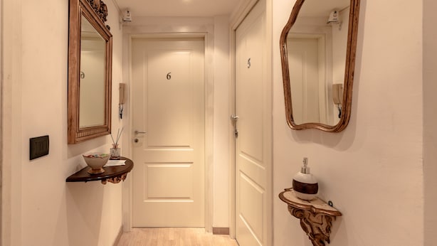 A hallway with a door labeled '6', a wooden console table with a bowl and a vase, and a wall-mounted mirror. - Aiello Rooms (Milan)