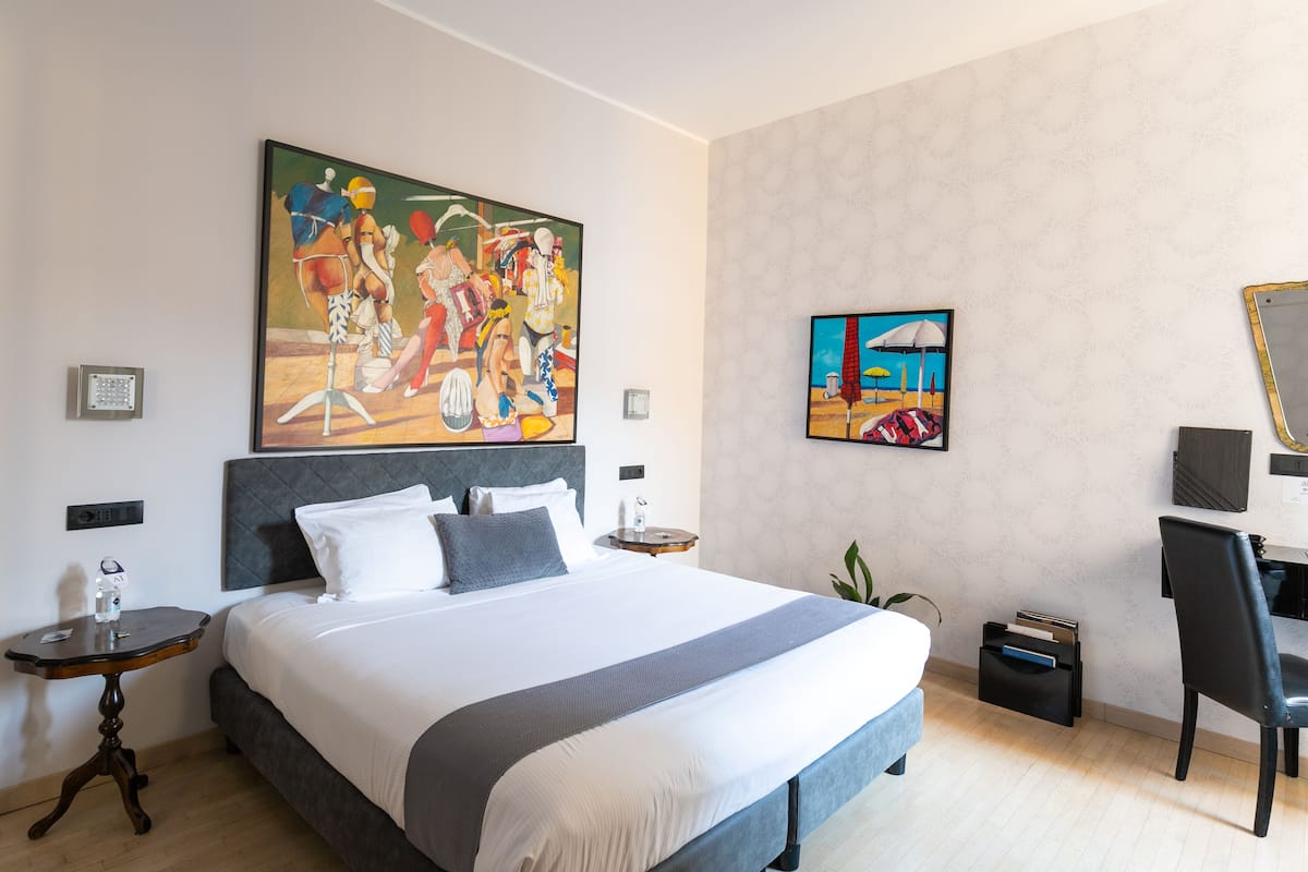 A hotel room with a large bed, a desk, and two paintings on the walls.