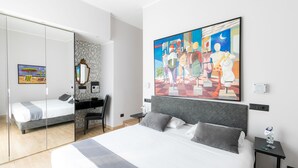 A modern hotel room with a large bed, a desk, and a chair. There is a painting on the wall and a mirror on the door. - Aiello Rooms (Milan)