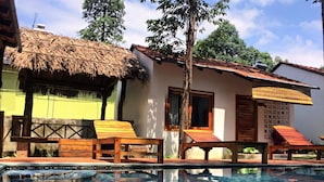 Una piscina con sillas de descanso y una estructura de techo de paja.