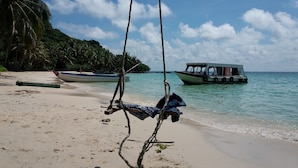 Una playa con una silla hamaca, un bote y una isla boscosa al fondo.