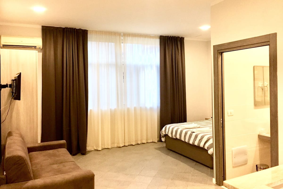 A hotel room with a bed, a sofa, a TV, and a bathroom.