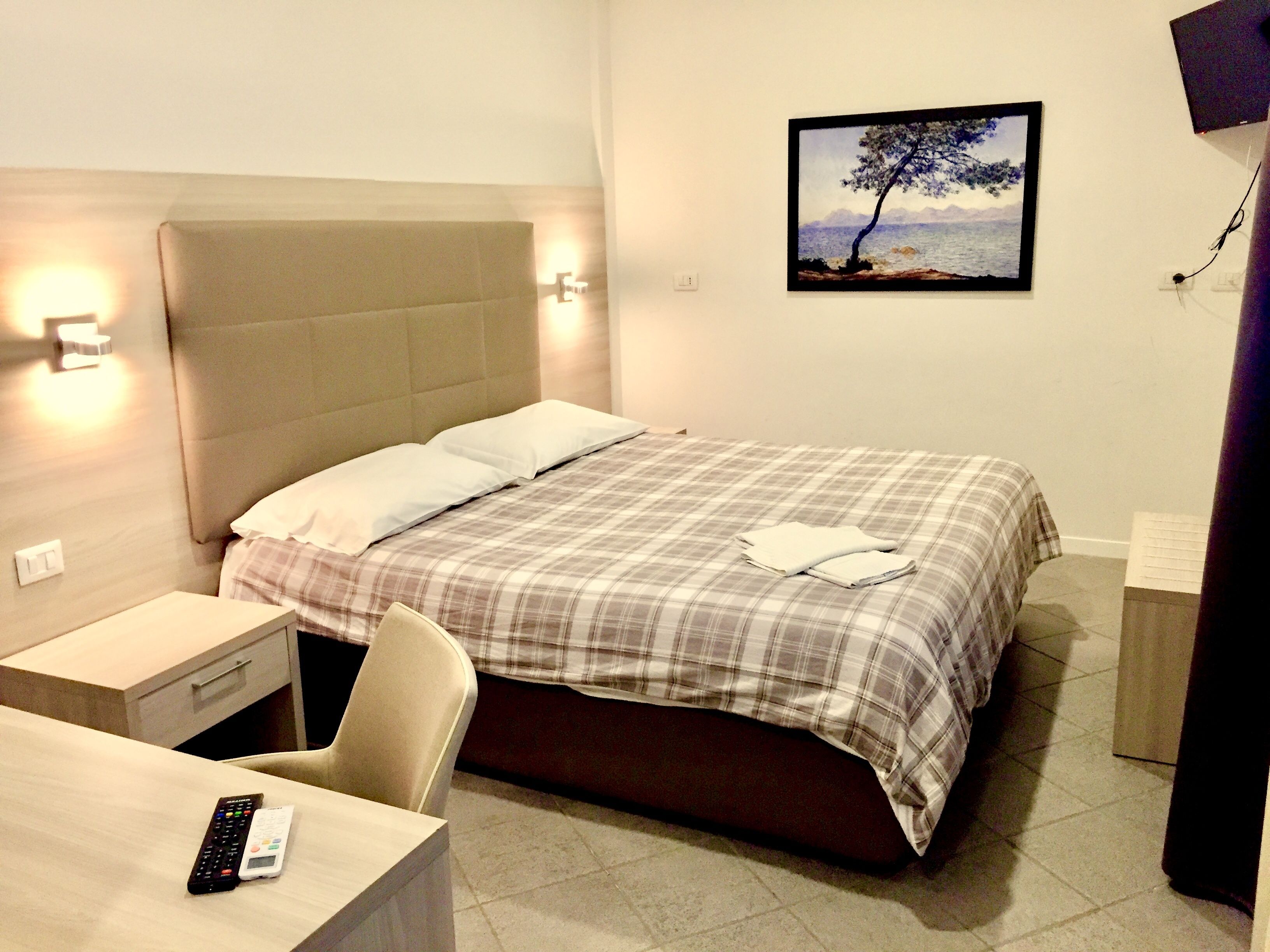 Una habitación de hotel con cama, mesita de noche, silla y un cuadro en la pared.