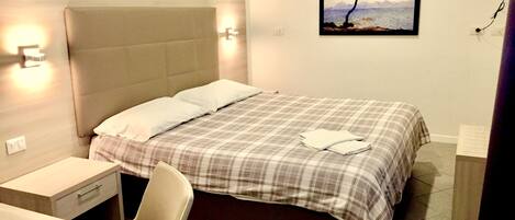 A hotel room with a bed, bedside table, chair, and a painting on the wall.