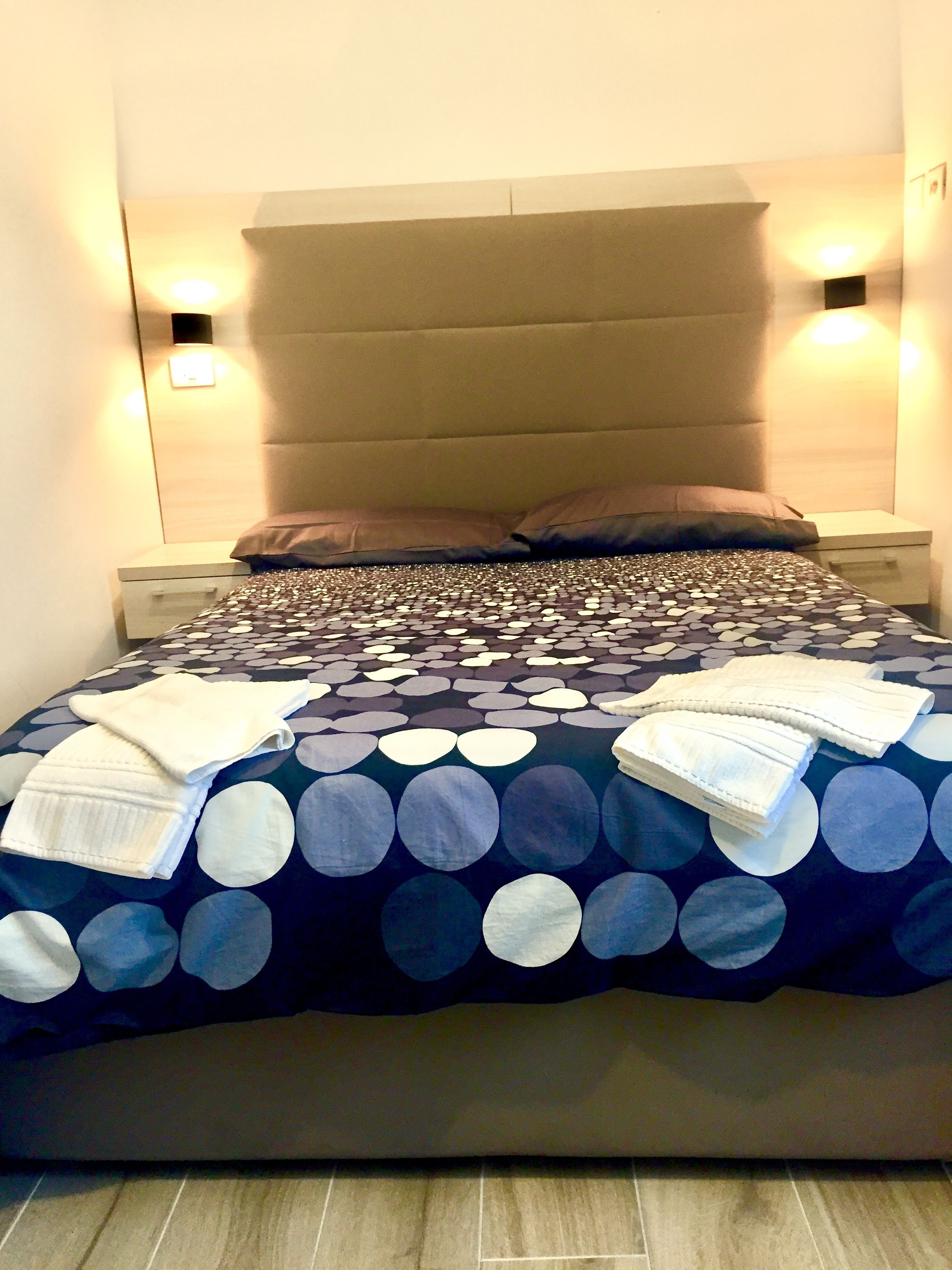 A neatly made bed with a patterned bedspread, two pillows, and a bedside table with a lamp.