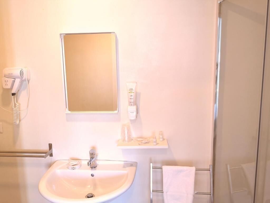 A bathroom with a sink, mirror, hairdryer, and towel rack.