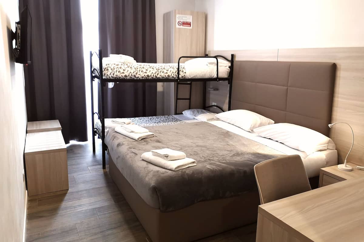 A bunk bed with a grey mattress, a bedside table, a desk, and a chair.