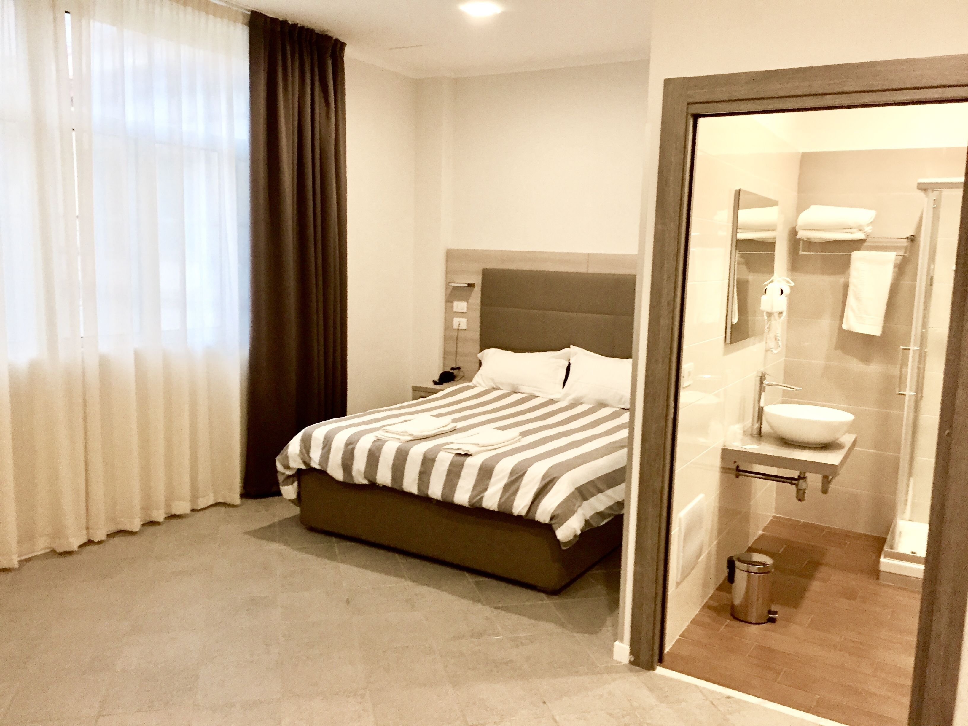 Una habitación de hotel con cama, mesita de noche, espejo y baño con lavamanos e inodoro.