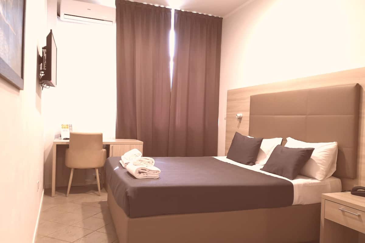 A hotel room with a bed, a desk, a chair, and a nightstand.