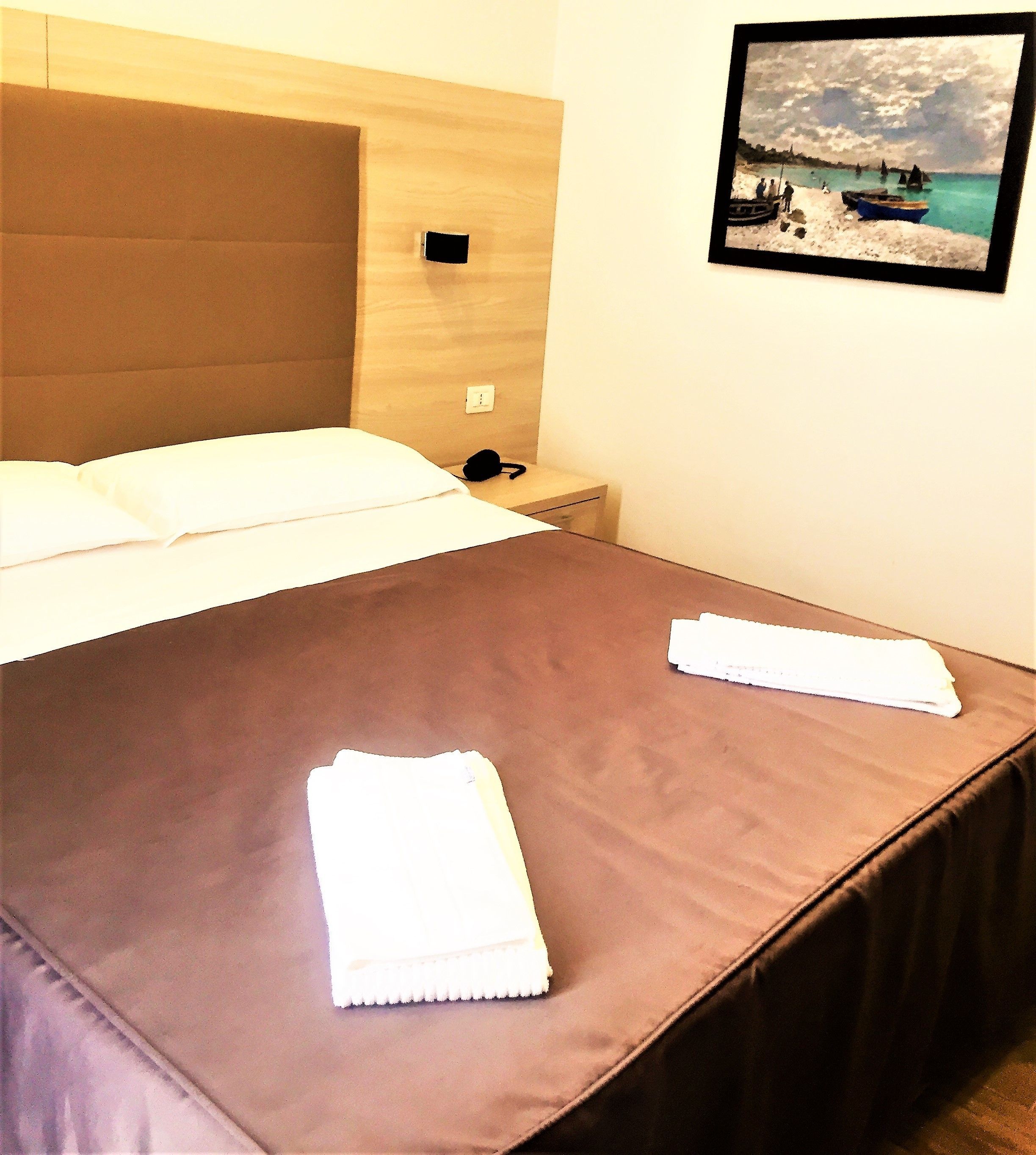 Una camera d'hotel con un letto, un comodino, un quadro appeso alla parete e un asciugamano bianco sul letto.