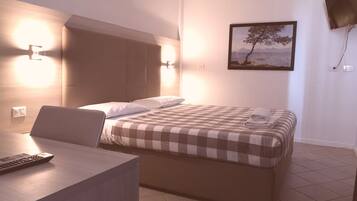 A hotel room with a bed, a desk, a chair, a wall-mounted TV, and a painting of a tree.