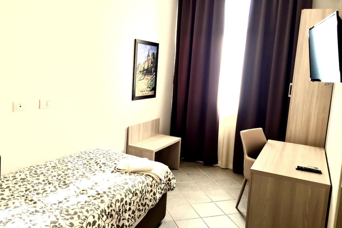A hotel room with a bed, a desk, a chair, a TV, and a window with curtains.