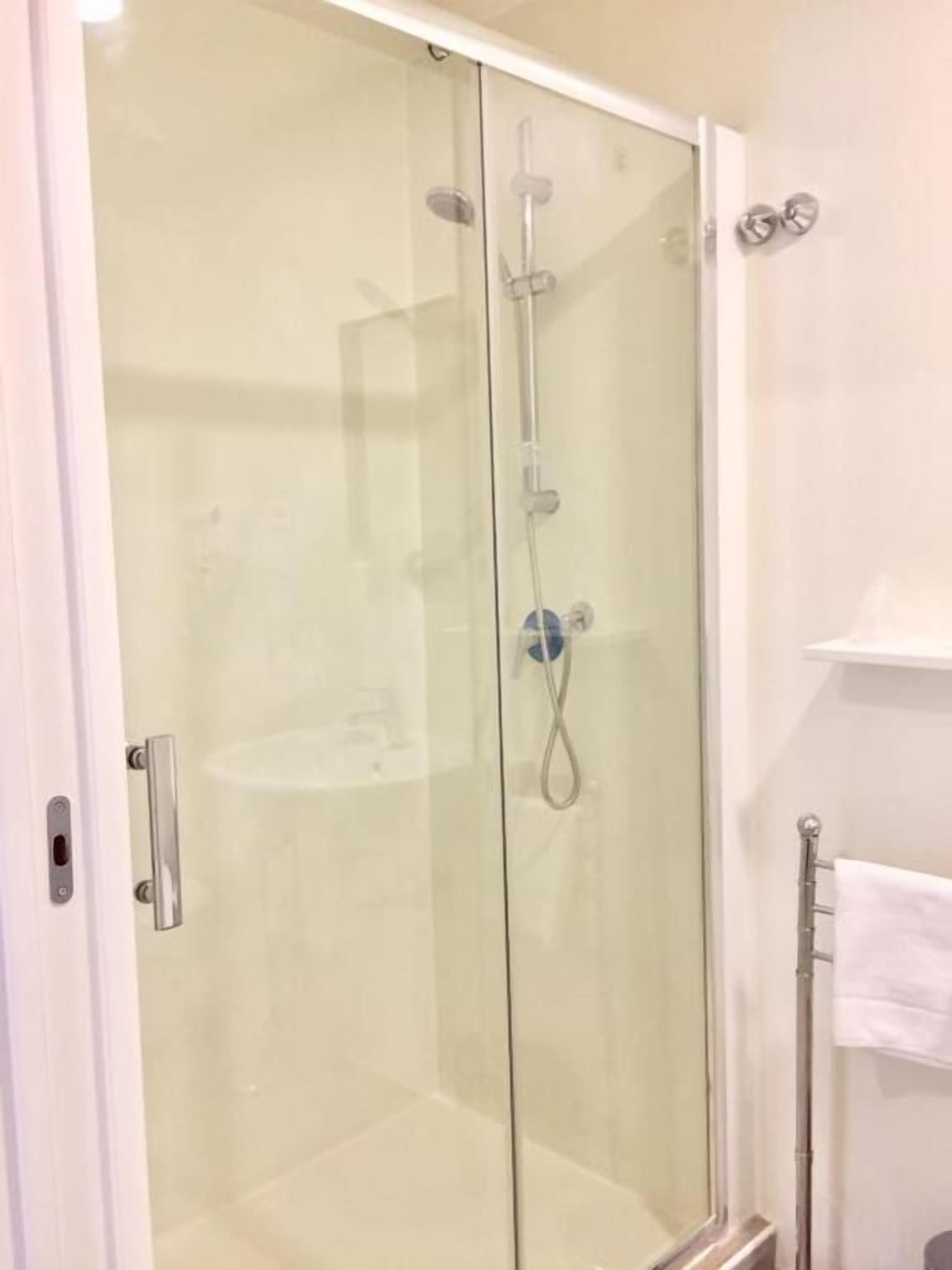 A glass-enclosed shower stall with a handheld showerhead and a wall-mounted faucet.