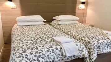 A double bed with a patterned bedspread and two pillows, a bedside table with a lamp, and a wall-mounted light fixture.
