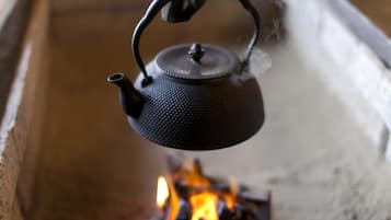 A close-up of a black metal kettle with a textured surface and a handle, suspended over a fire with visible flames.