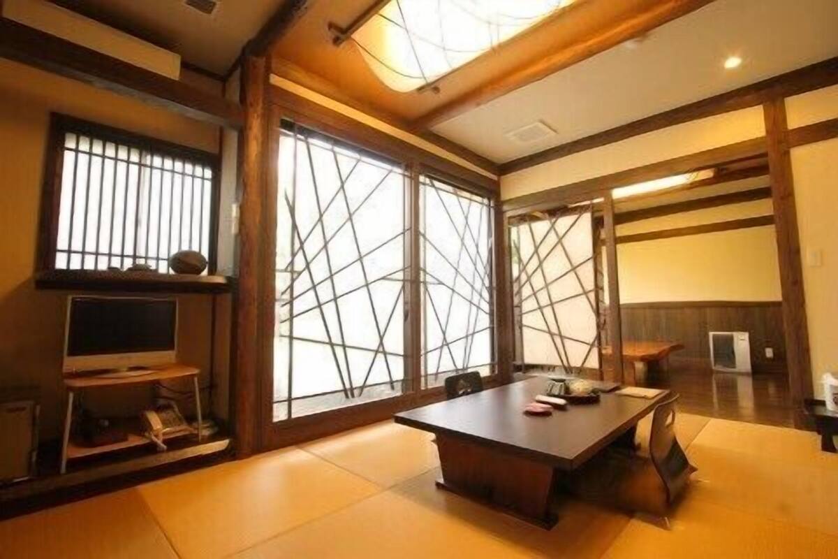 A traditional Japanese room with tatami flooring, a low table, a TV, and sliding doors.