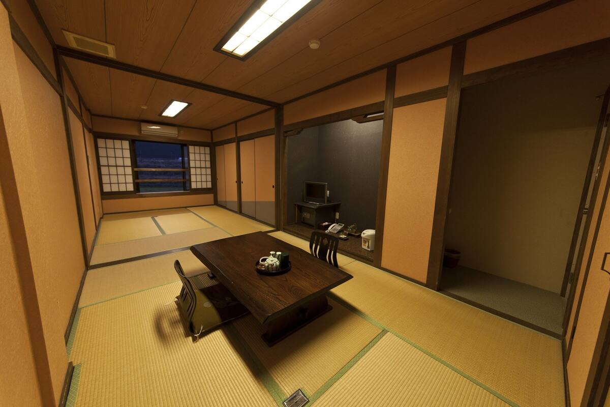 A traditional Japanese room with tatami flooring, a low table with a tea set, a television, and sliding doors.