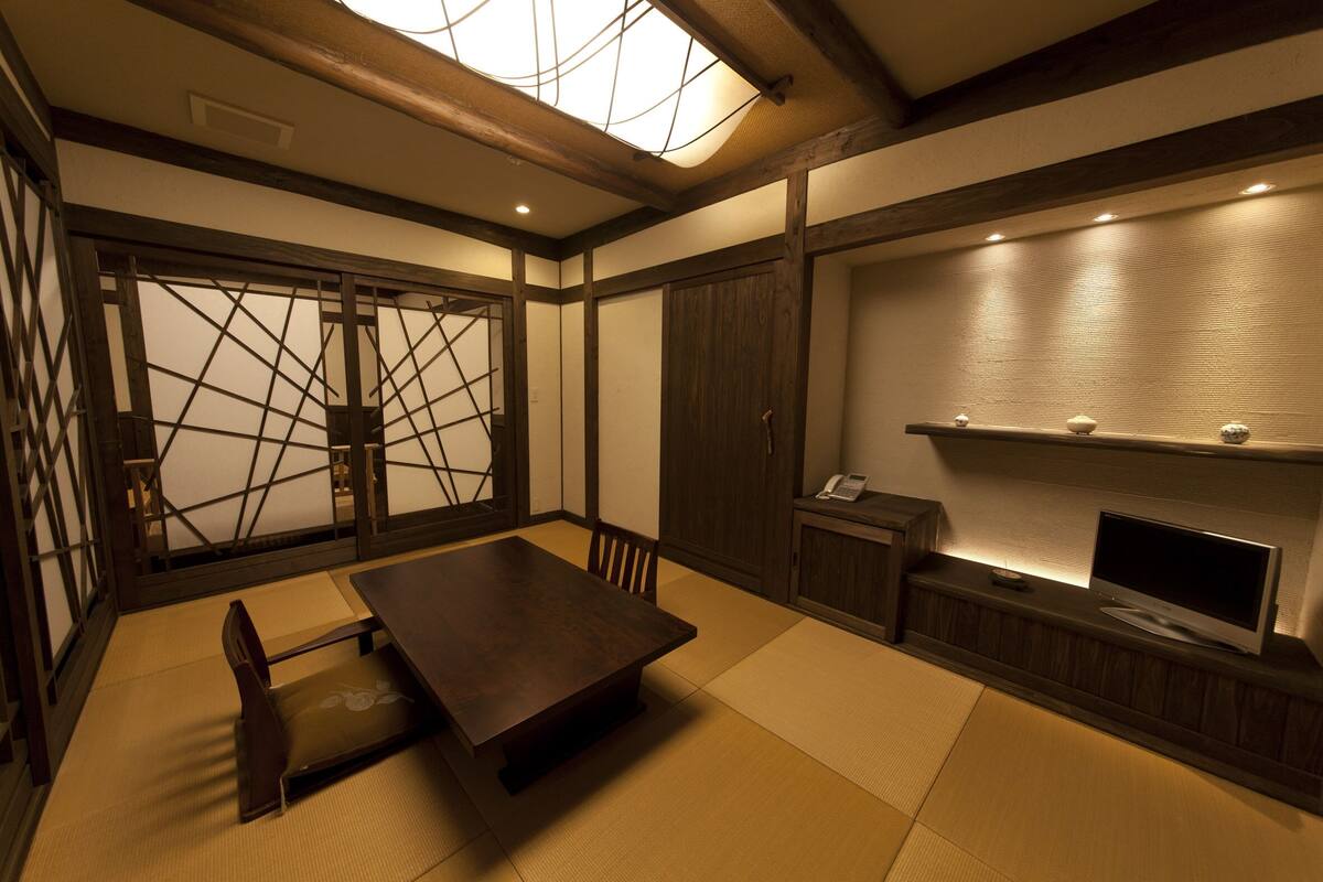 A traditional Japanese room with tatami flooring, a low wooden table, a TV on a wooden stand, and sliding doors with a lattice design.