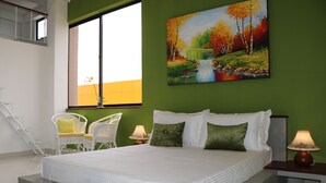 A bedroom with a large bed, two bedside tables, a window with a view of a building, and a painting on the wall. - Golf Link Colombo (Colombo)
