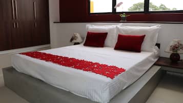 A neatly made bed with a white and red bedspread, a wooden wardrobe, and a nightstand with a lamp.