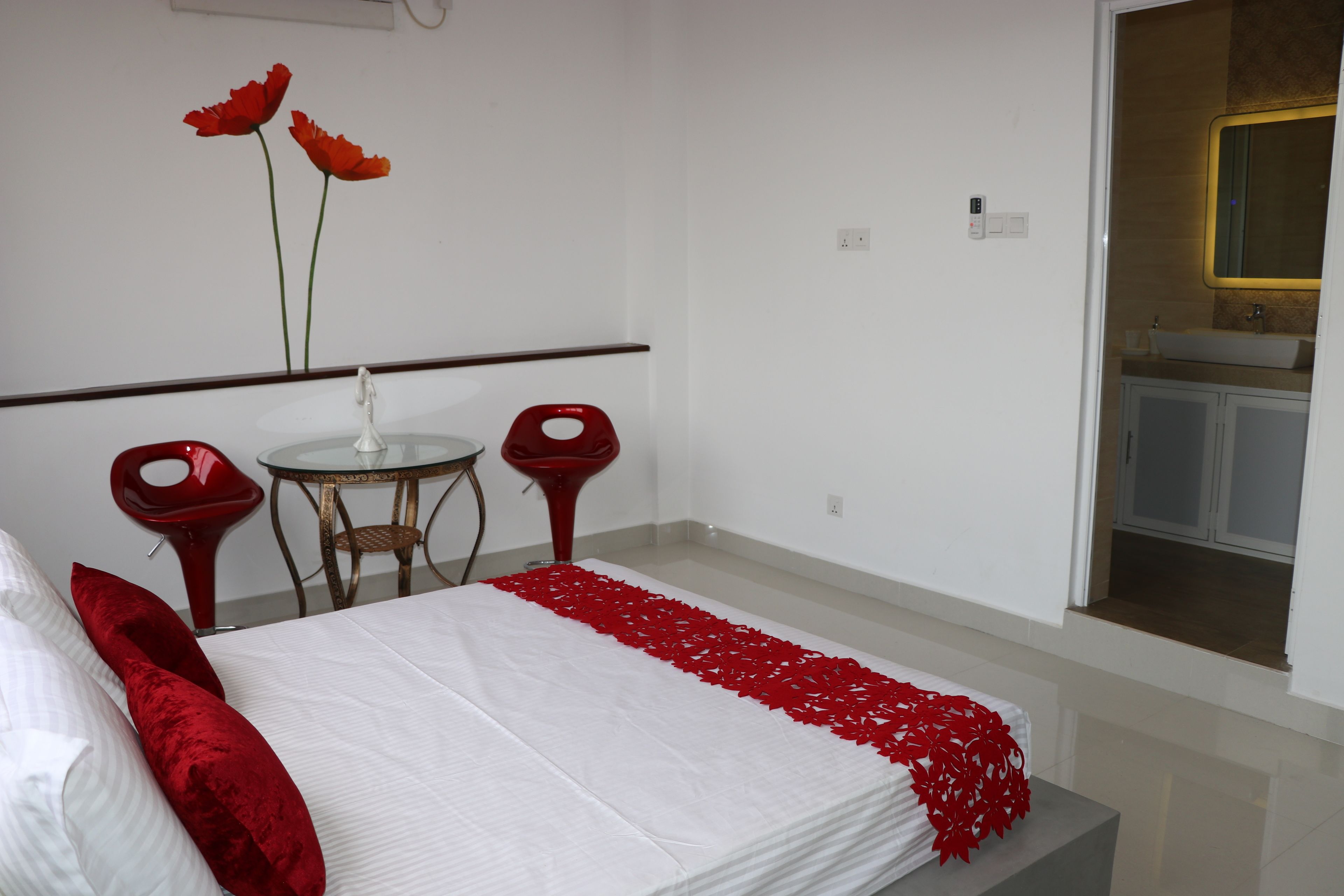 A bedroom with a bed, a small round table, two red chairs, and a bathroom visible through an open door.