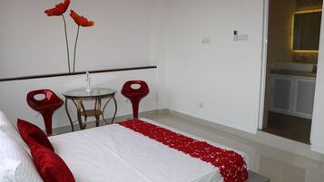 A bedroom with a bed, a small round table, two red chairs, and a bathroom visible through an open door.