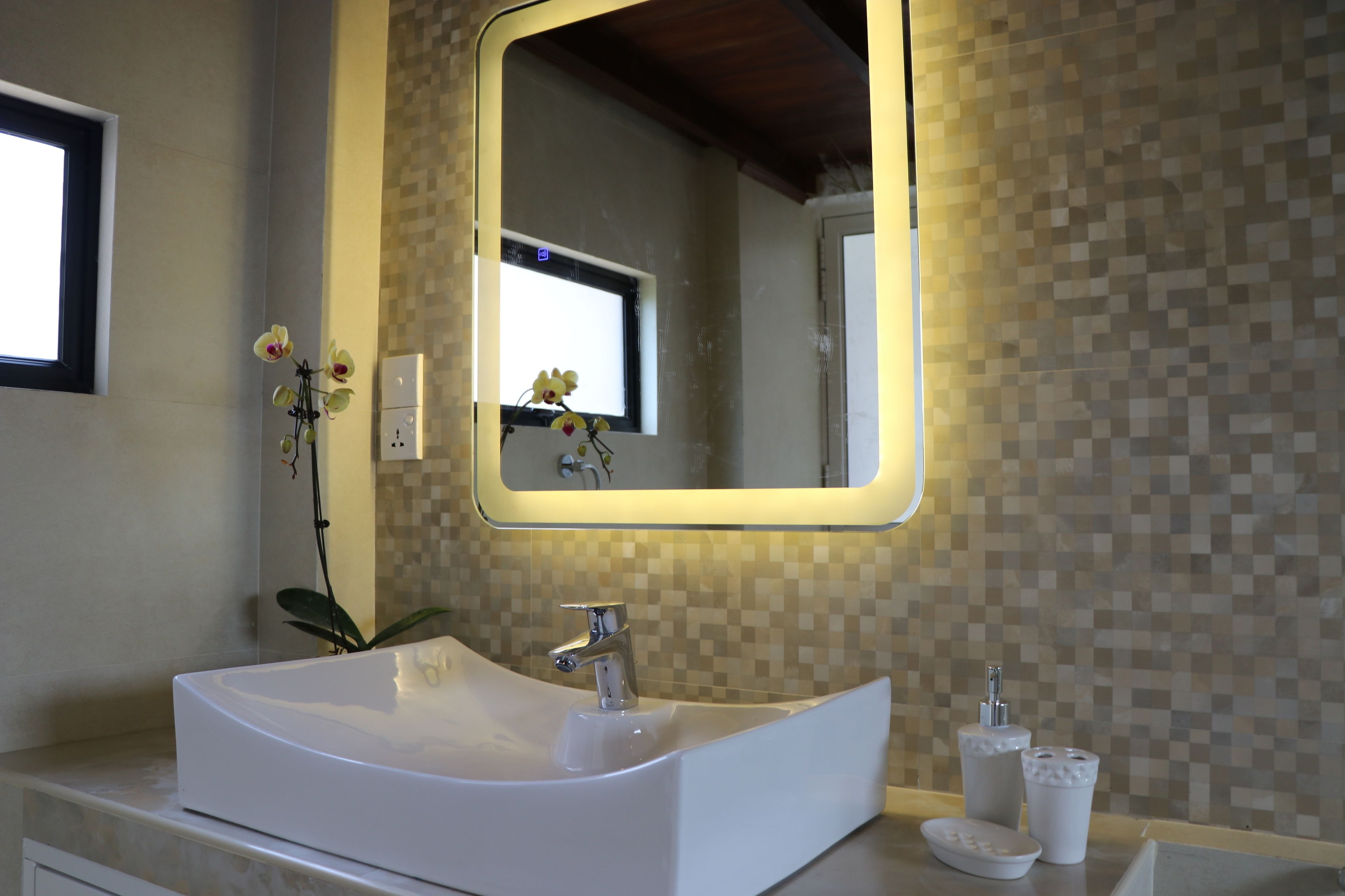 Un baño con lavamanos blanco, espejo y pared de azulejos.