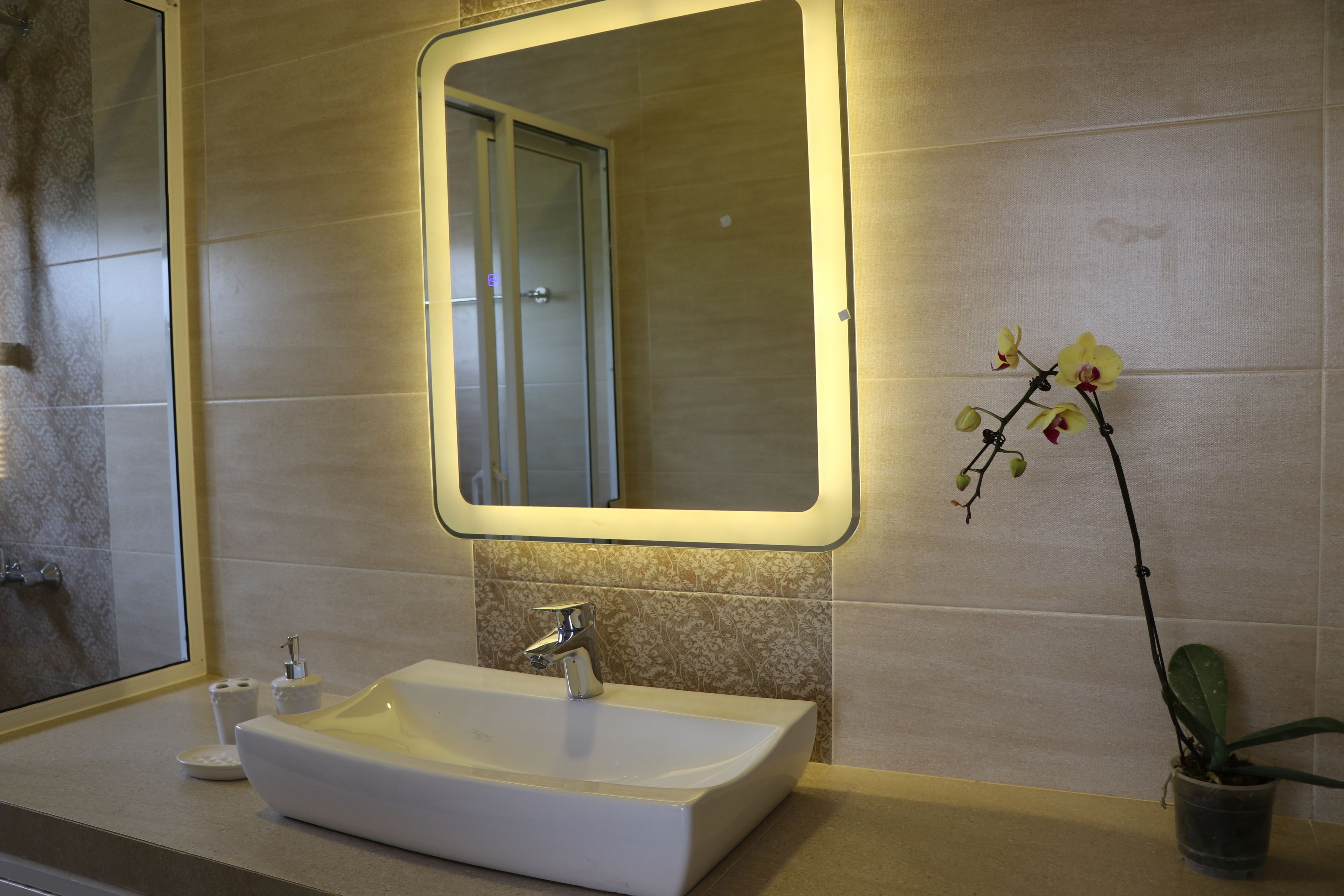 Ein Badezimmer mit einem weißen Waschbecken, einem Spiegel und einer Orchidee im Blumentopf.