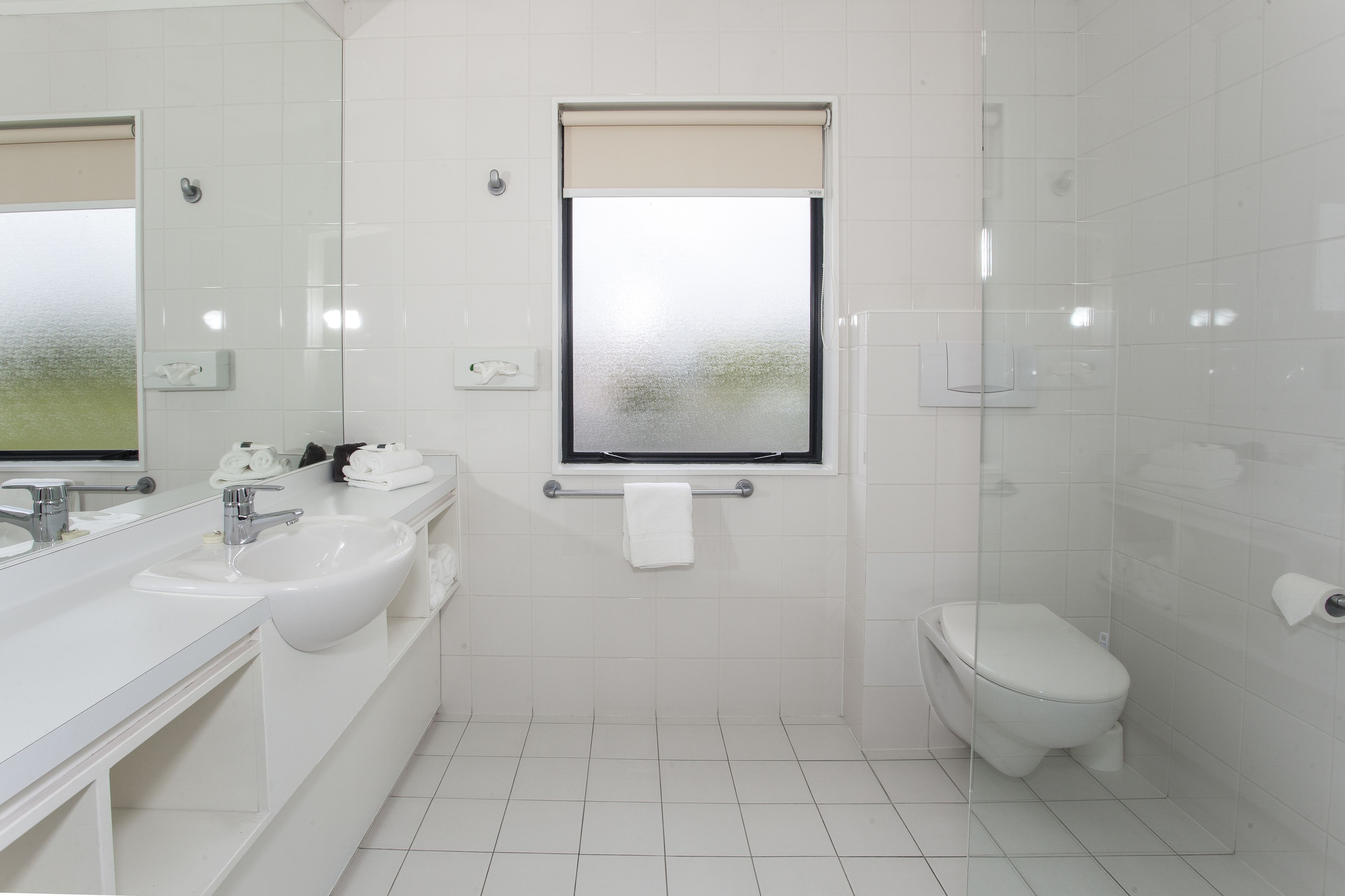 A modern bathroom with a large mirror, two sinks, a toilet, and a shower enclosure.