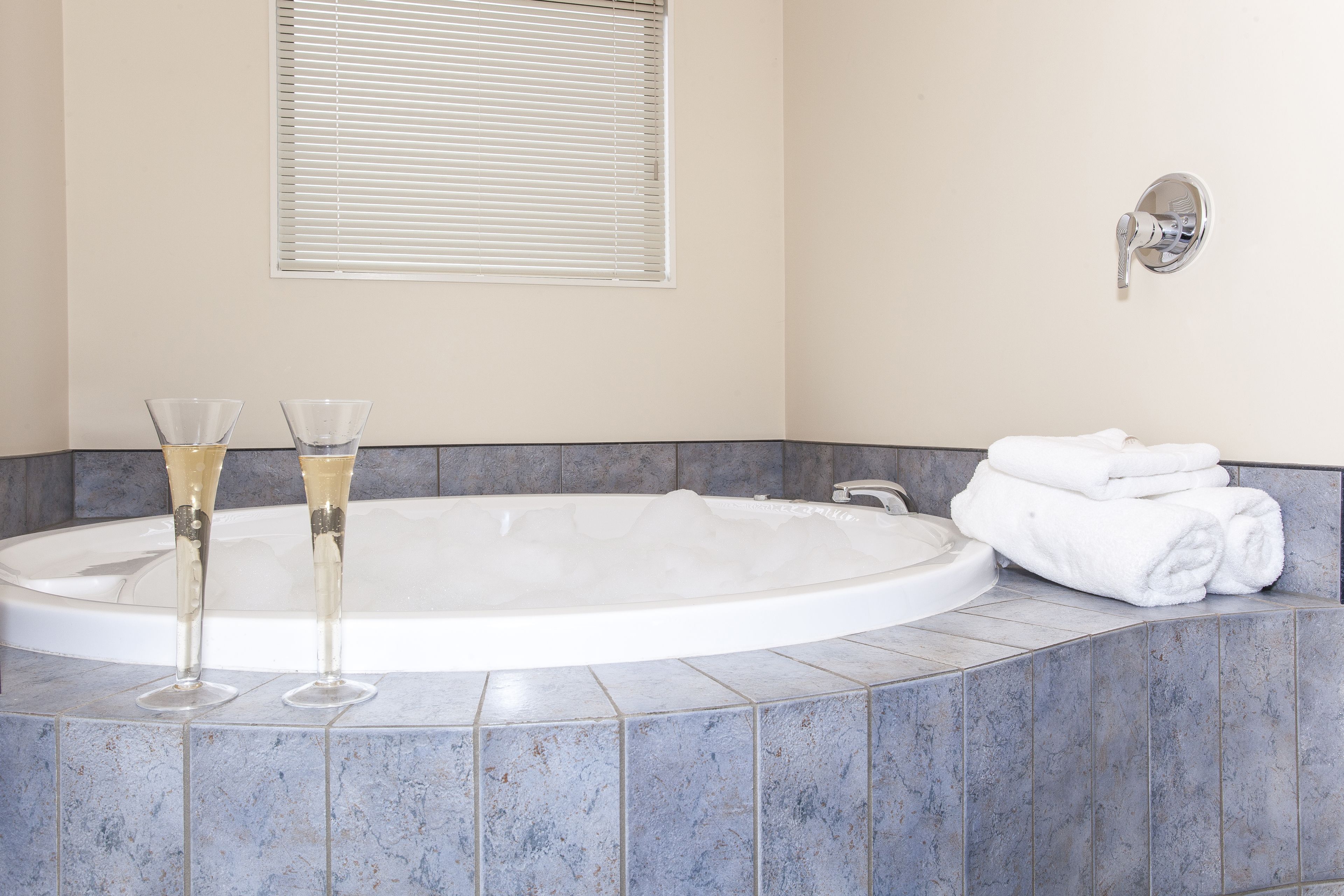 A bathroom with a large bathtub, two champagne glasses, and a stack of white towels.