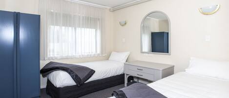 A hotel room with two beds, a wardrobe, a desk, and a window with sheer curtains.