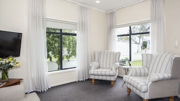 Una habitación con alfombra gris, dos sillones, un sofá, un televisor y una mesita con un jarrón de flores.