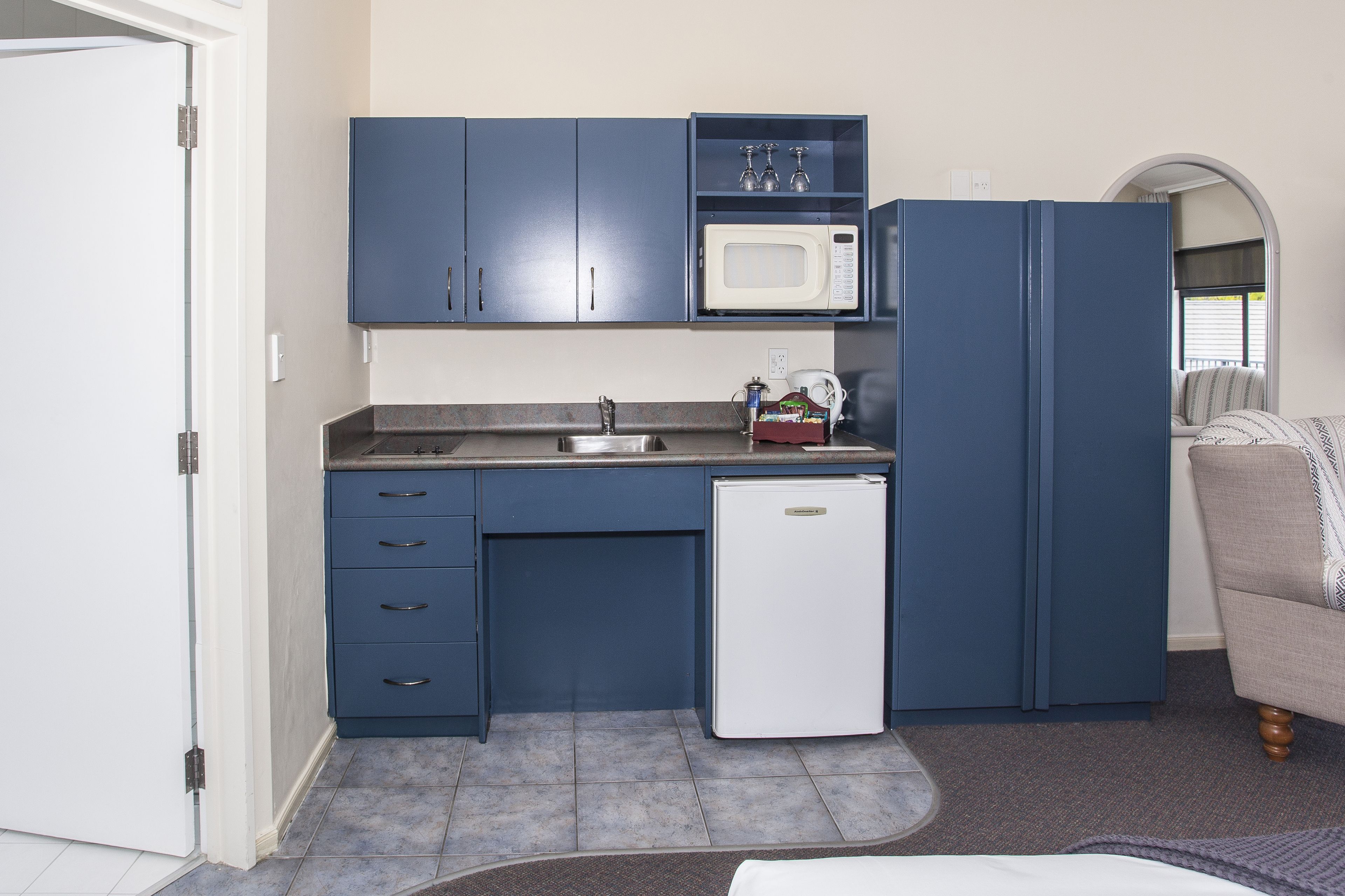 A compact kitchen with blue cabinets, a microwave, a small refrigerator, and a sink.