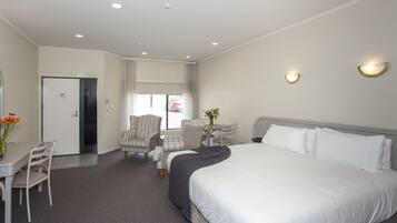 A hotel room with a large bed, a desk with a chair, a small table with a vase, and a chair.