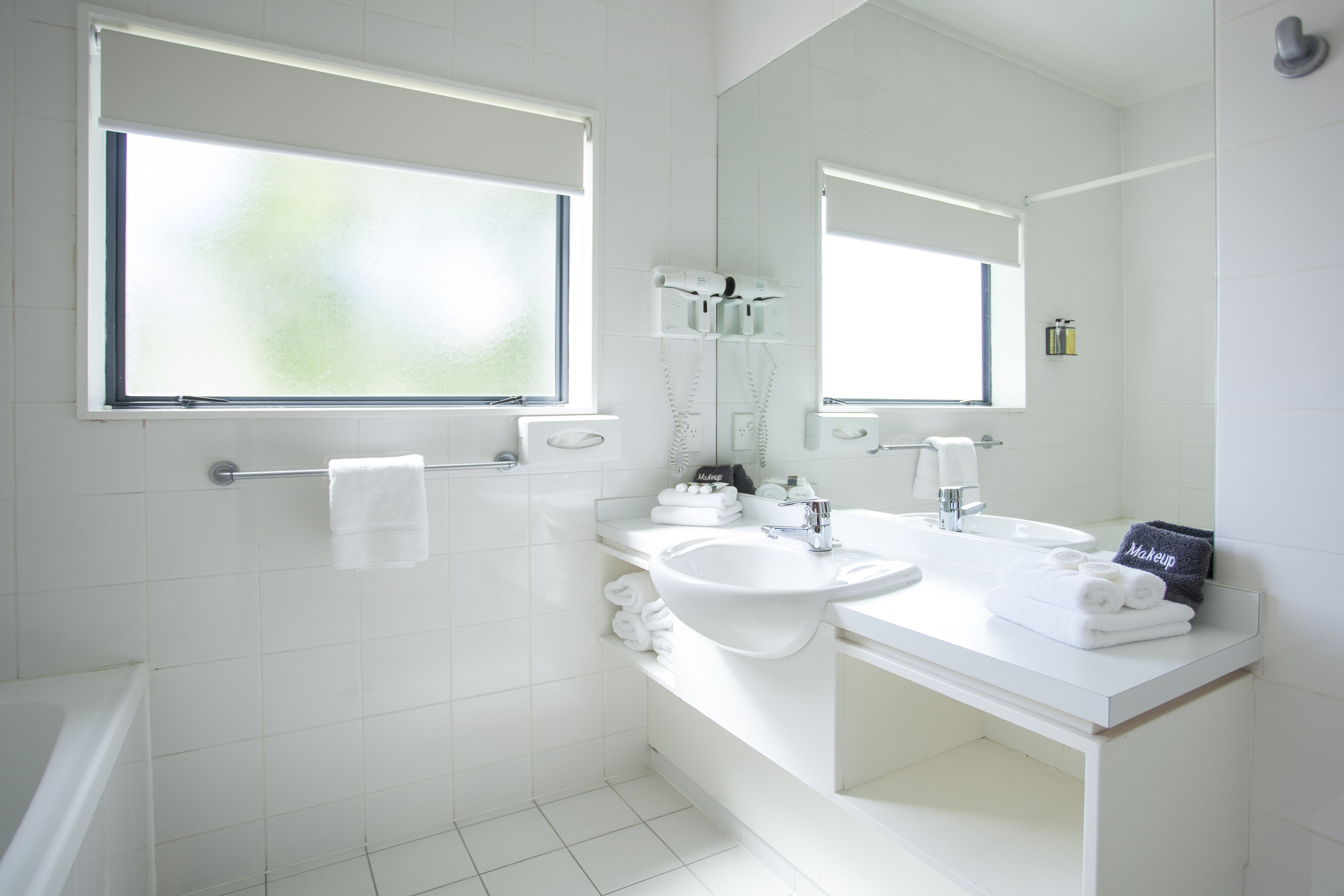 Un baño moderno con sanitarios blancos, un espejo grande y una ventana.