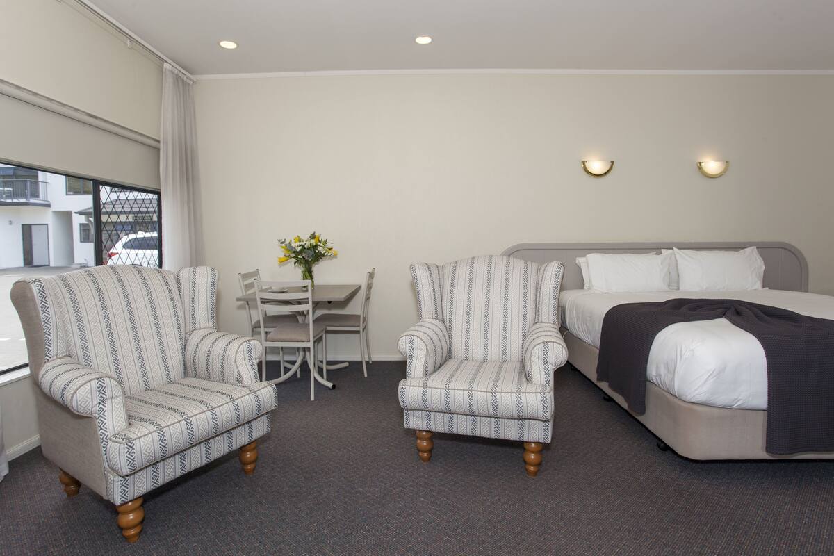 A hotel room with a bed, two armchairs, a small table with chairs, and a vase of flowers.