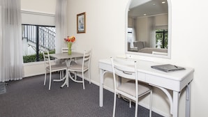 Habitación de hotel con un escritorio blanco, dos sillas, un espejo grande y una ventana con cortinas.