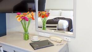Habitación de hotel con escritorio, espejo, un jarrón con flores, libreta, teléfono y cama con una colcha a rayas blanco y negro.