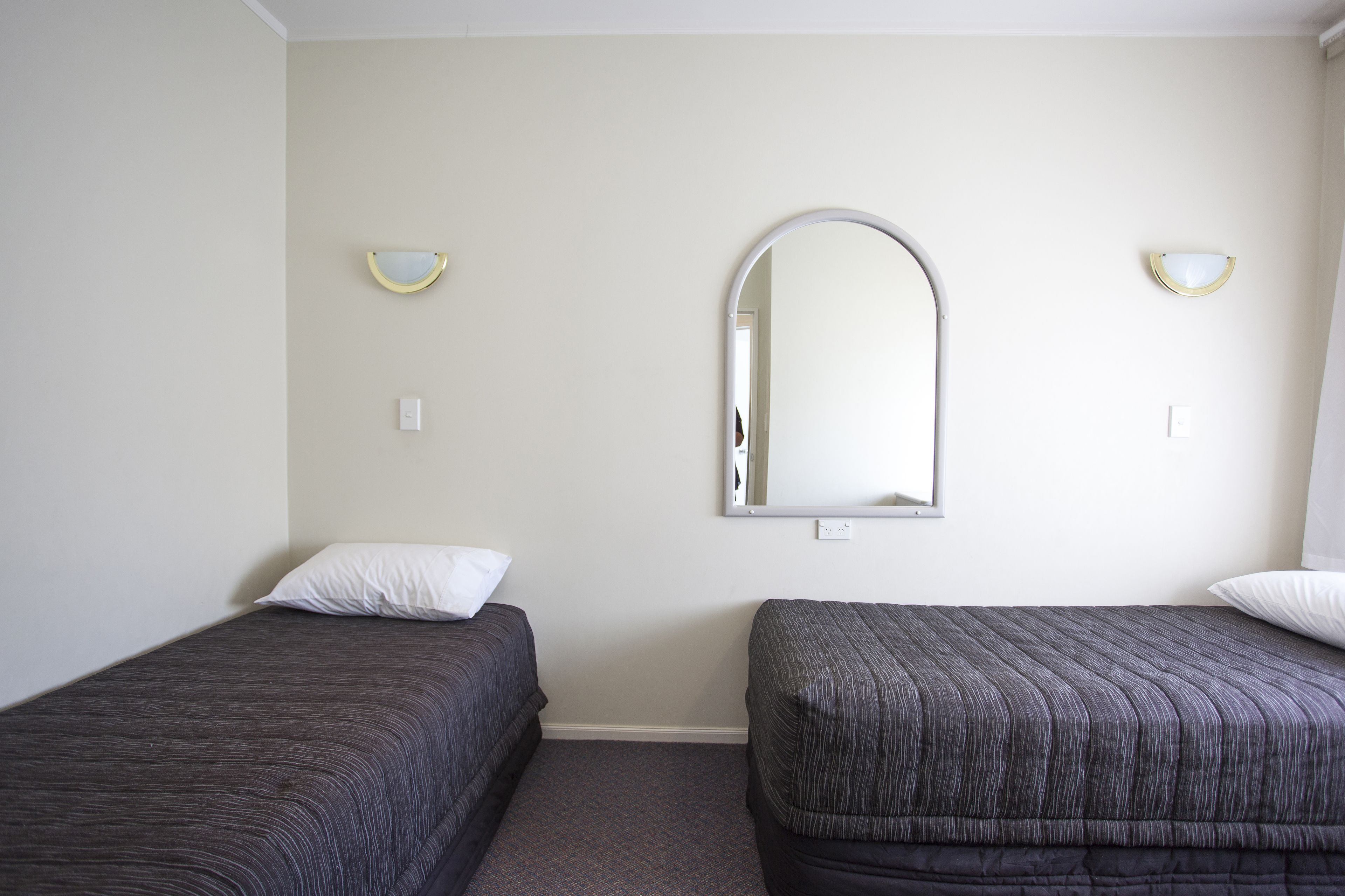 Ein Zimmer mit zwei Einzelbetten, einem großen Spiegel und zwei Wandleuchten.