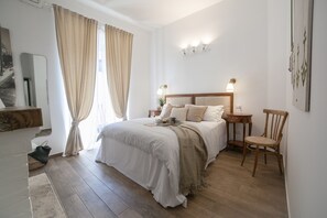 A bedroom with a large bed, wooden flooring, a wooden chair, and a nightstand with a lamp. - Maison Coquette (Rome)