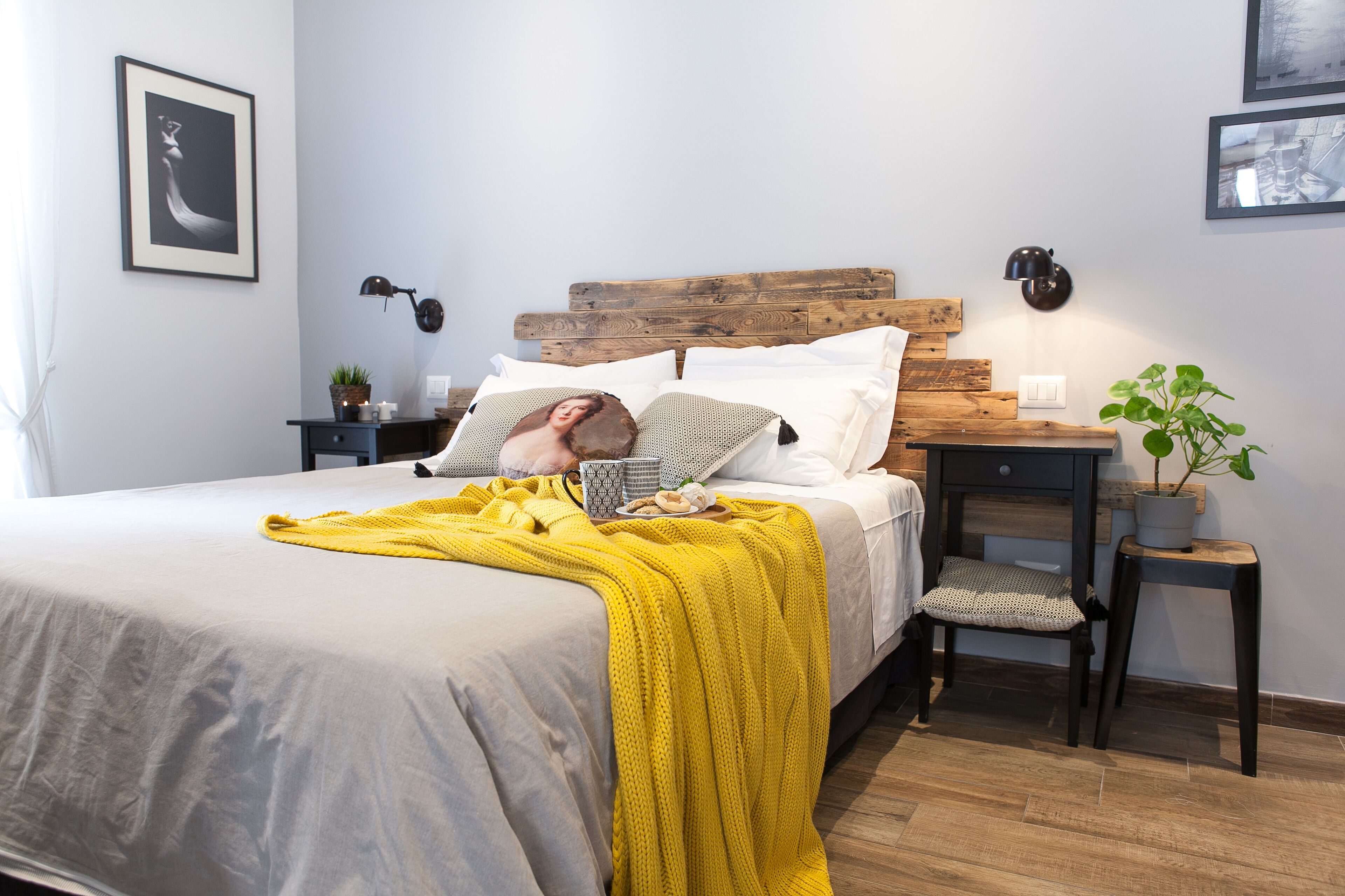 A neatly made bed with a yellow blanket, a bedside table with a lamp, and a small potted plant.
