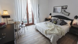 A bedroom with a bed, bedside tables, a desk, a chair, and a balcony.