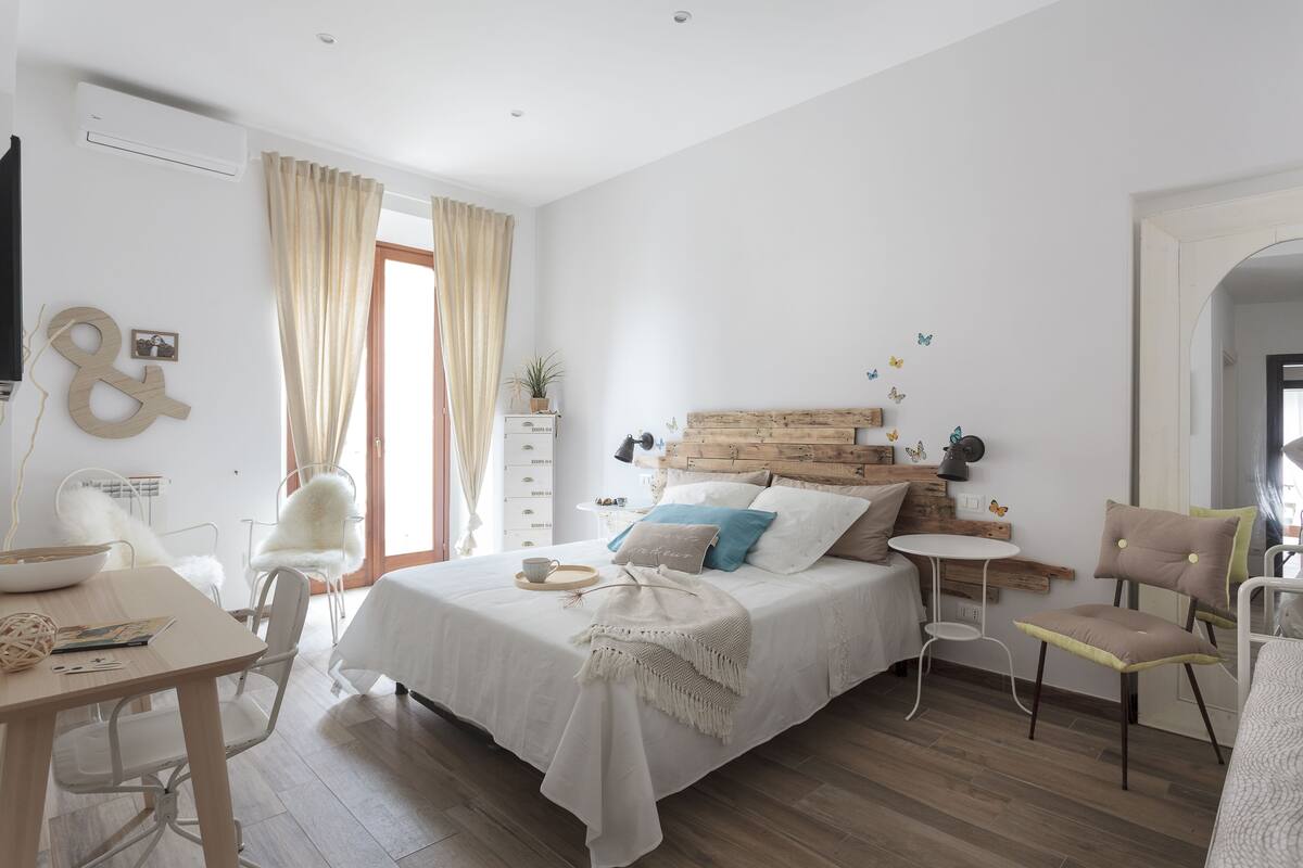 A bedroom with a bed, bedside table, chair, and a small table with a lamp.