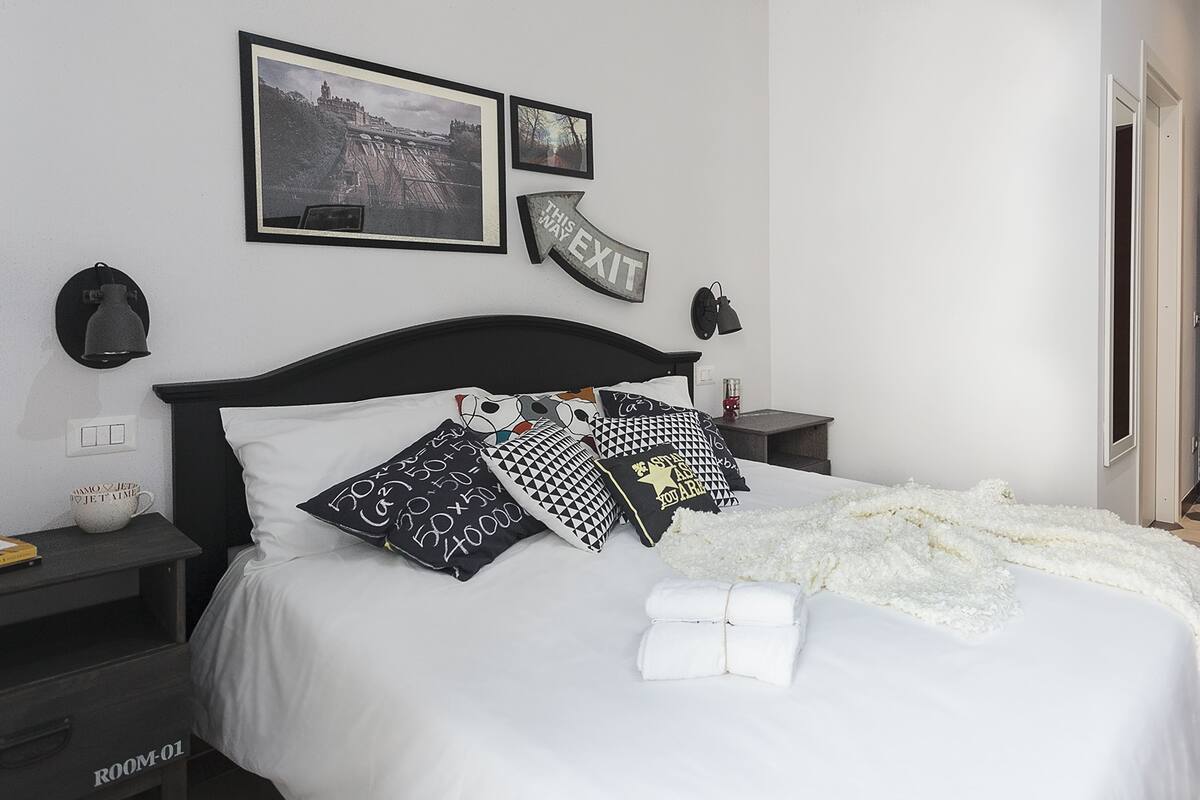 A neatly made bed with multiple pillows, a white blanket, and a sign indicating an exit.