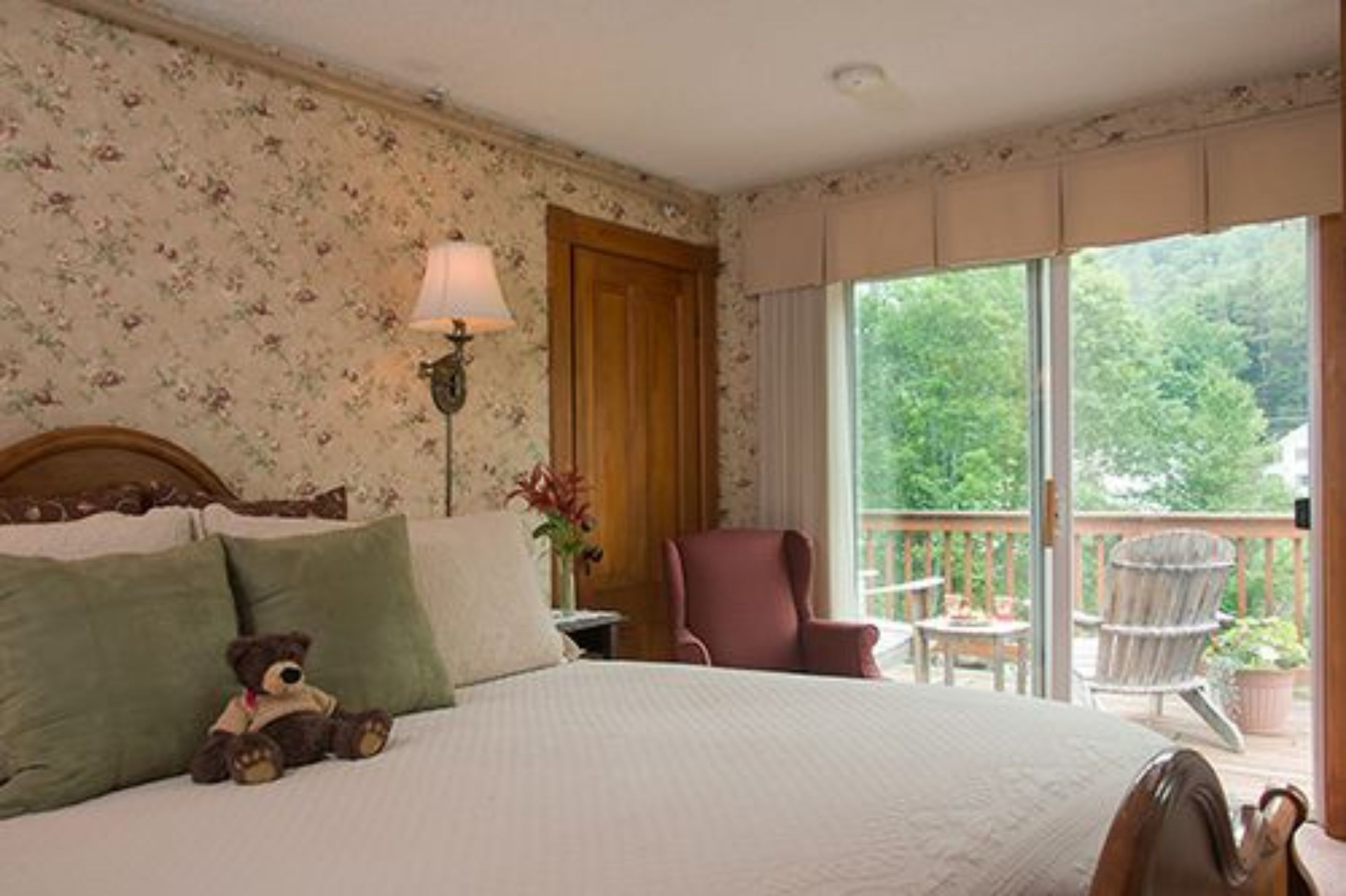 A bedroom with a bed, a chair, a lamp, and a view of the outdoors.