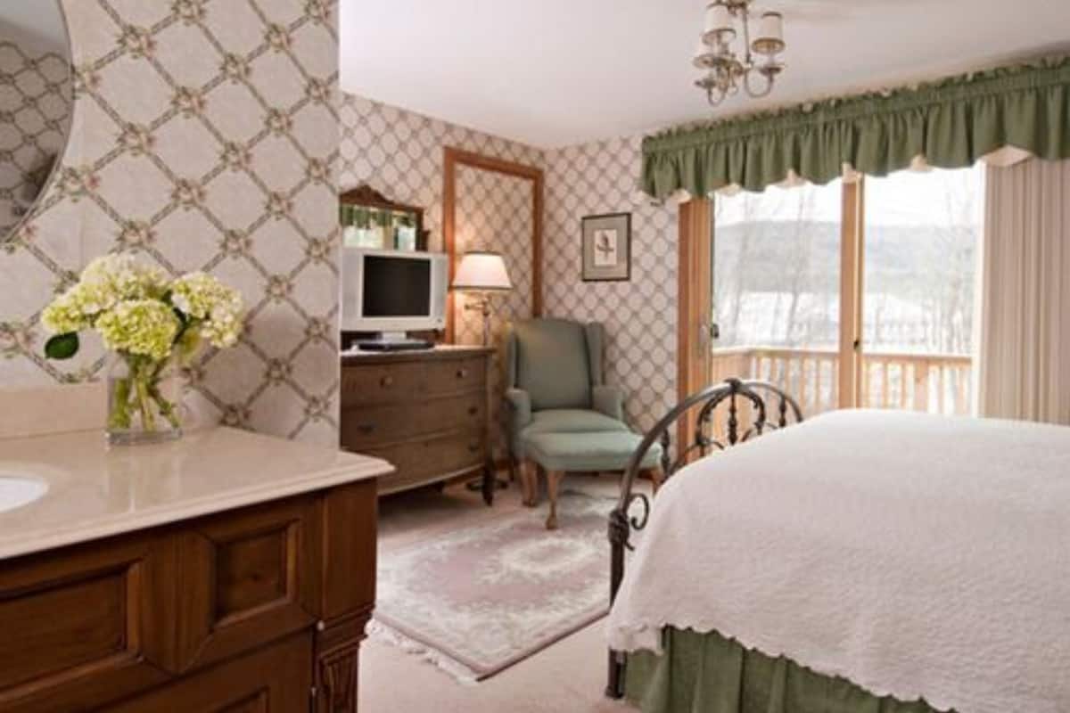 A bedroom with a bed, dresser, vanity, and a television.