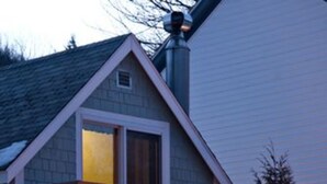 A two-story house with a balcony and a deck, surrounded by snow and illuminated by string lights. - Inn at Ellis River (Jackson)