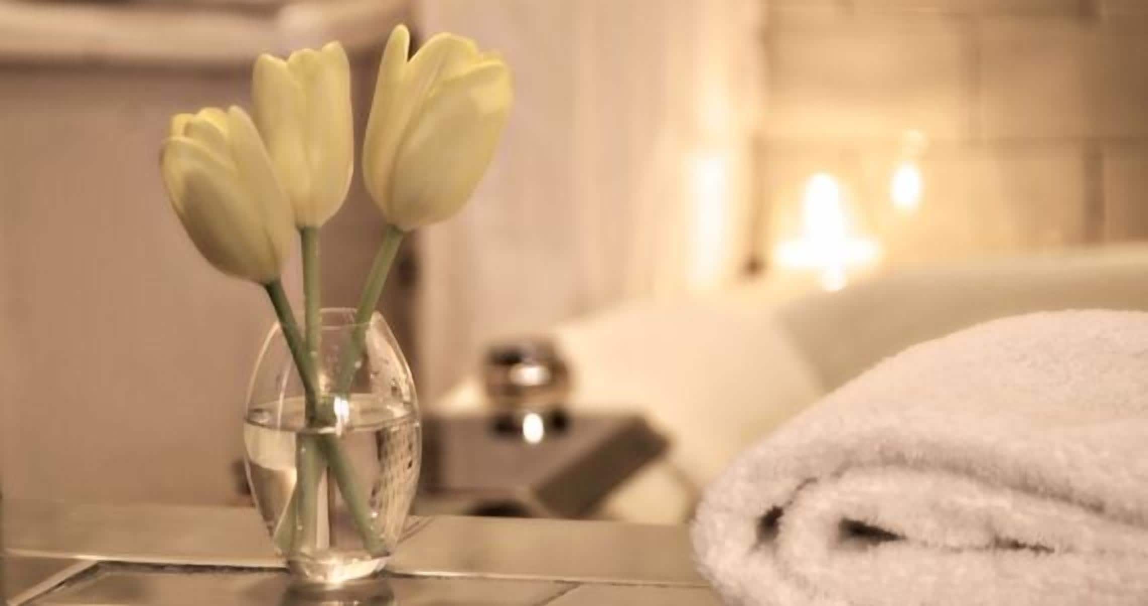 Un baño con un jarrón de tulipanes blancos sobre un mueble, una toalla blanca y una bañera.